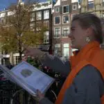 Thumbnail of http://“Puur%20gids%20wijst%20tijdens%20een%20stadsspeurtocht%20door%20de%20Amsterdamse%20grachten”%20“Vrolijke%20begeleider%20met%20oranje%20Puur-jas%20legt%20route%20uit%20tijdens%20citygame%20in%20Amsterdam”%20“Stadsgids%20vertelt%20over%20de%20Amsterdamse%20grachtenpanden%20tijdens%20een%20bedrijfsuitje”