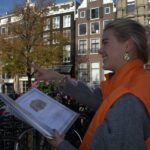 Thumbnail of http://“Puur%20gids%20wijst%20tijdens%20een%20stadsspeurtocht%20door%20de%20Amsterdamse%20grachten”%20“Vrolijke%20begeleider%20met%20oranje%20Puur-jas%20legt%20route%20uit%20tijdens%20citygame%20in%20Amsterdam”%20“Stadsgids%20vertelt%20over%20de%20Amsterdamse%20grachtenpanden%20tijdens%20een%20bedrijfsuitje”